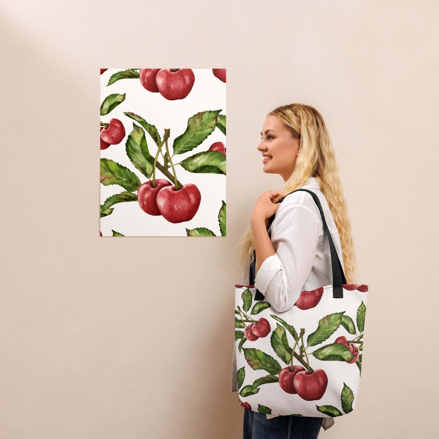 Woman holding an Orchard Bloom Cherry Canvas Tote bag featuring vibrant cherry blossom design against a floral wall art backdrop.