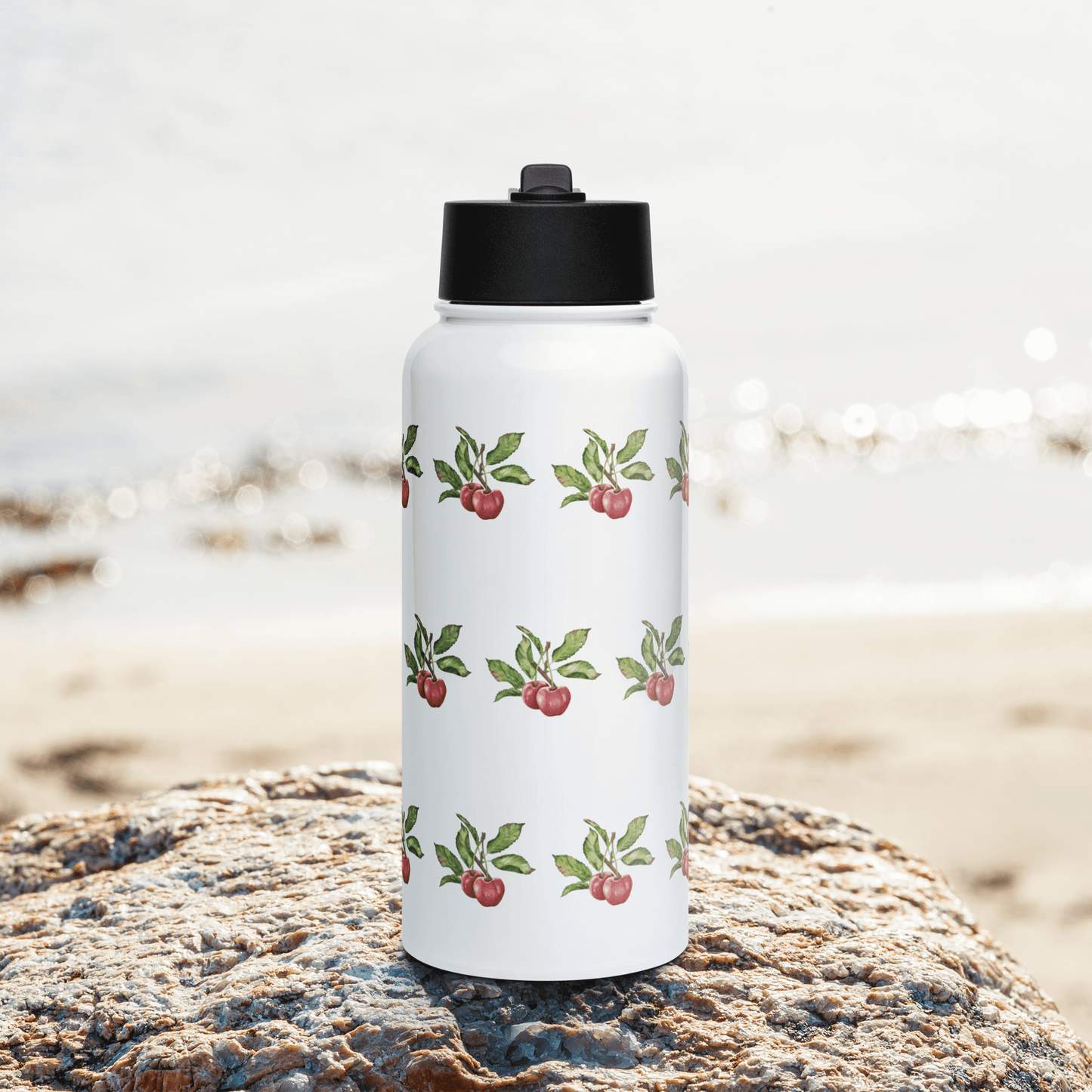 Bright cherry-patterned insulated tumbler on a rock by the beach, perfect for hydration and unique gifting.