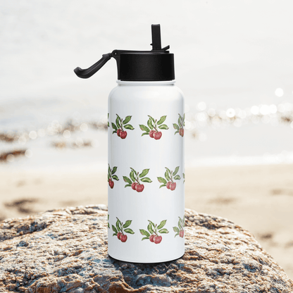 Bright Cherry insulated tumbler on a rock by the beach, showcasing its vibrant cherry design and convenient flip-top lid.