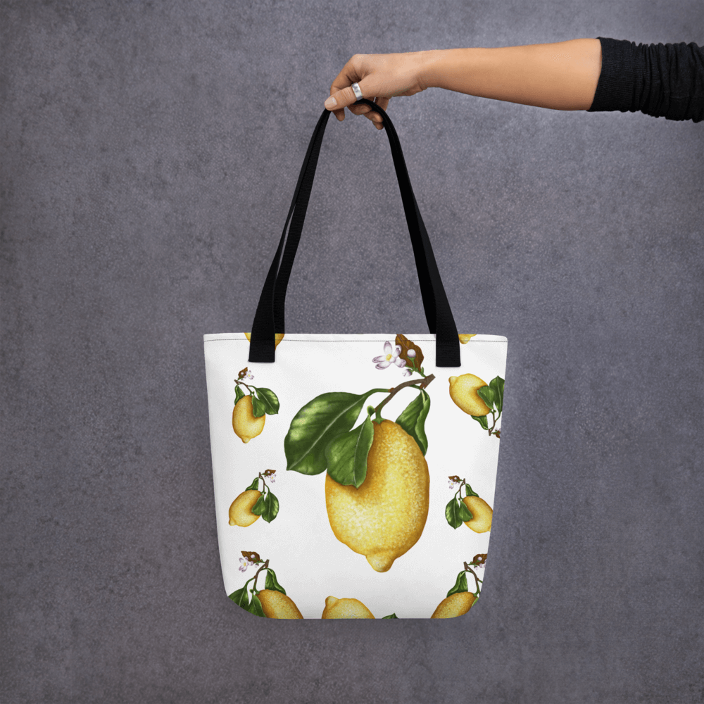 Lemon all-over print tote bag with black handles held by a hand holding it straight
