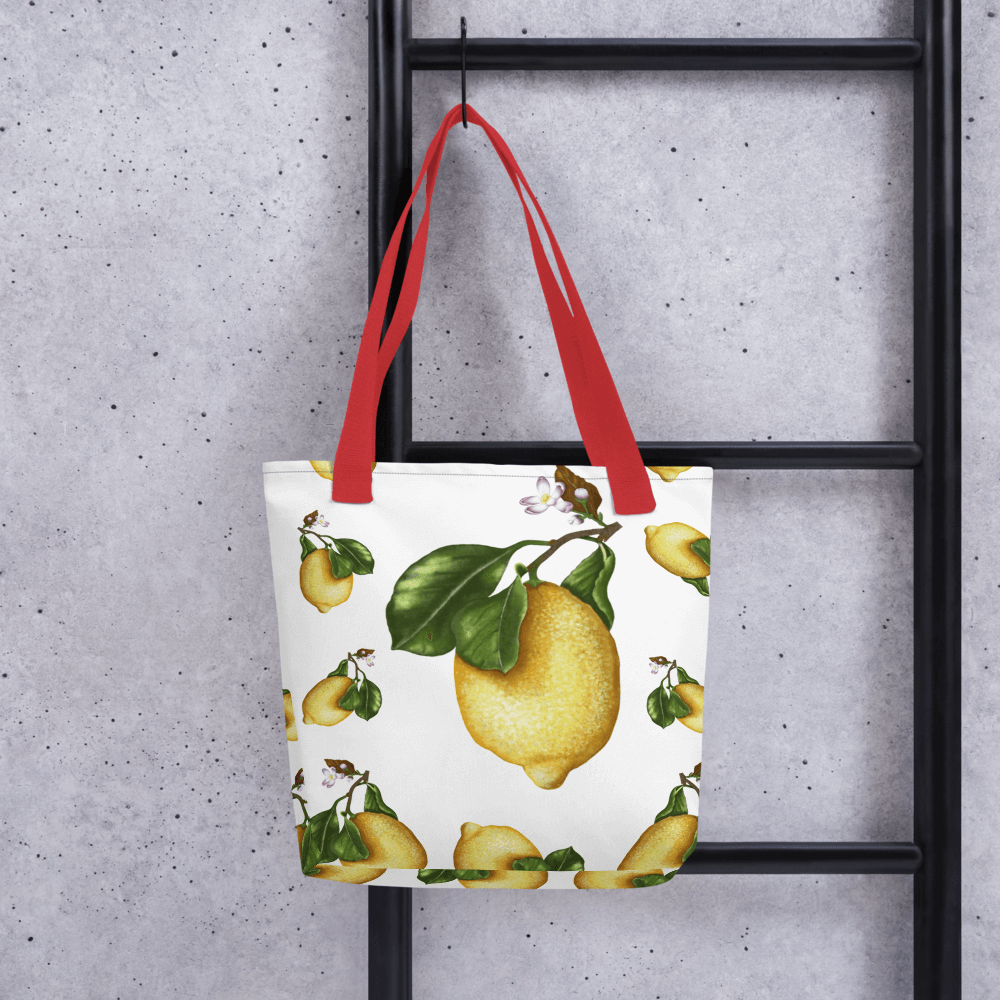 Lemon all-over print tote bag with red handles hanging on a ladder
