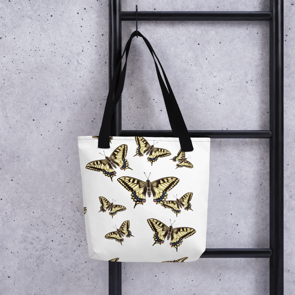 Machaon all-over print tote bag with black handles hanging on a ladder
