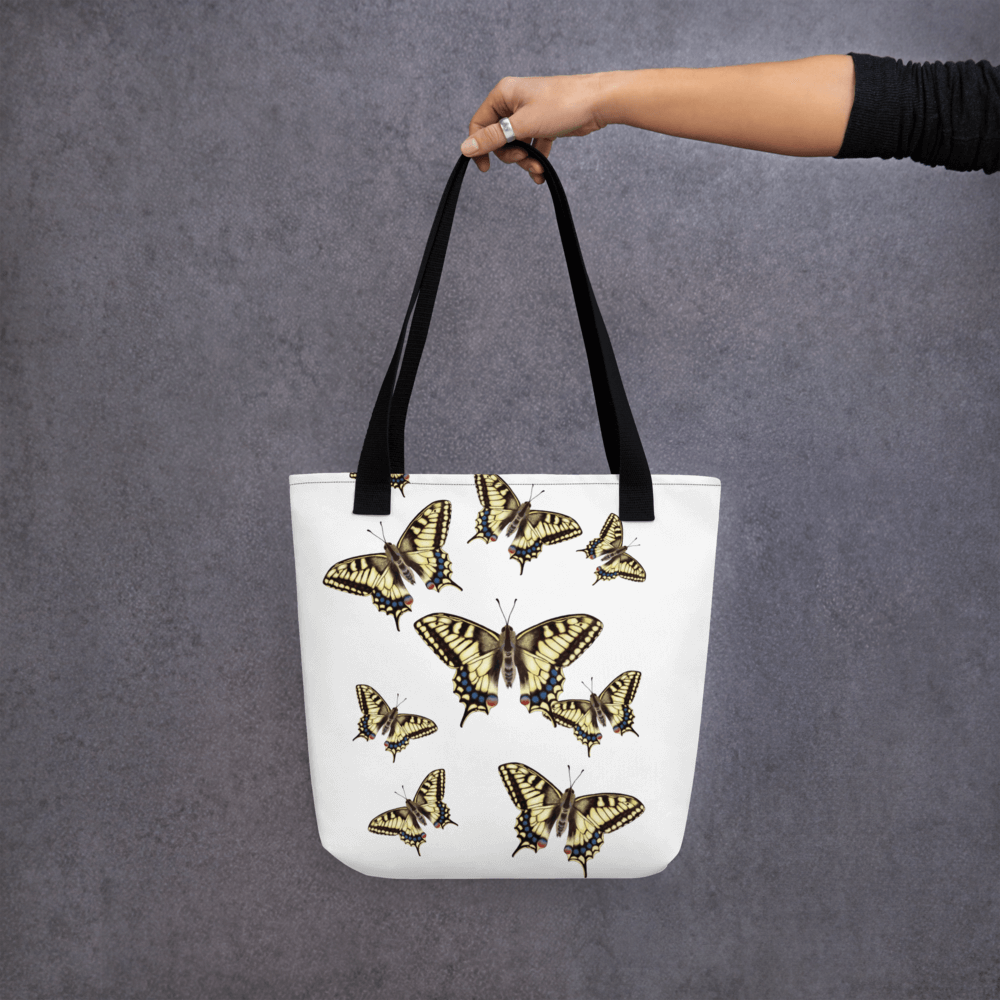 Machaon all-over print tote bag with black handles held by a hand holding it straight
