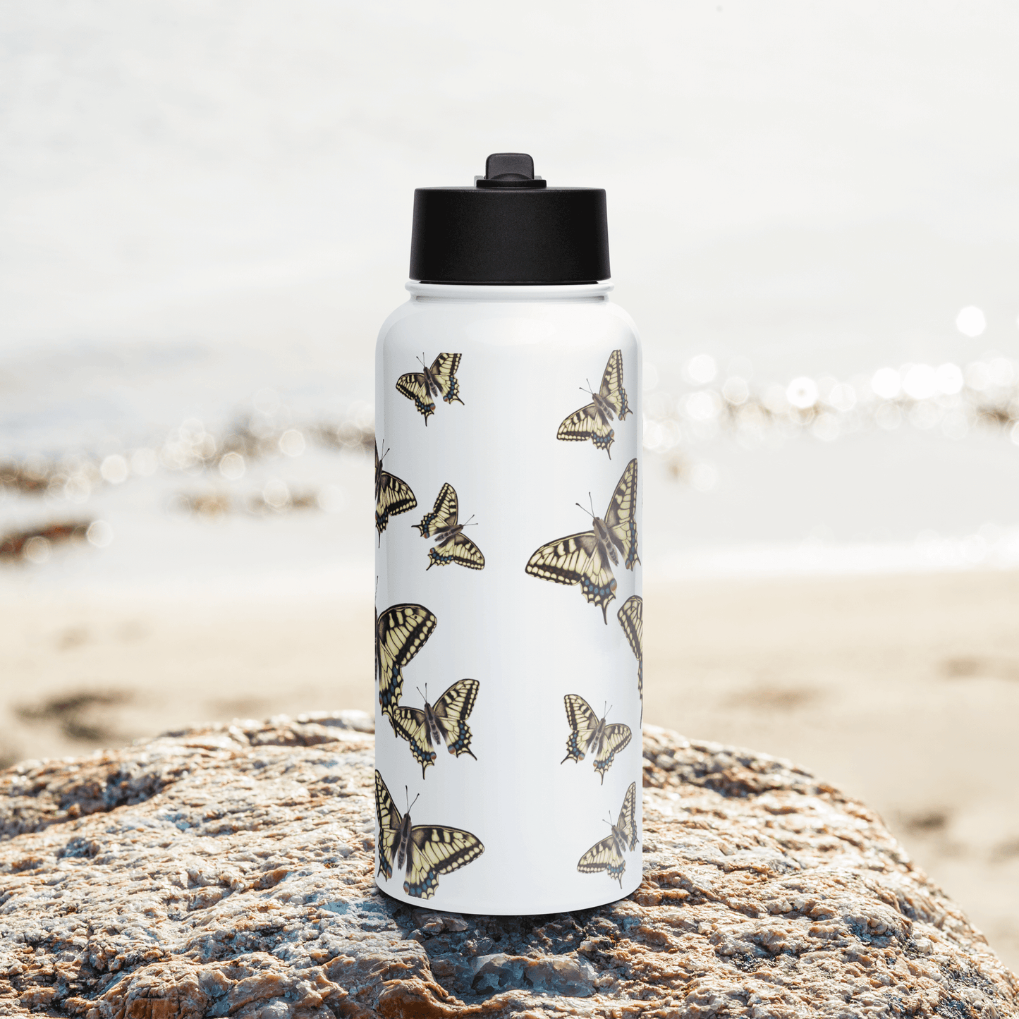 Personalized 950 ml stainless steel water bottle with Machaon Butterfly design on a rocky beach backdrop.