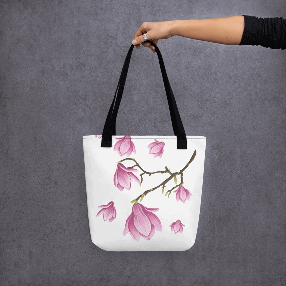 Magnolia all-over print tote bag with black handles held by a hand holding it straight from the other side