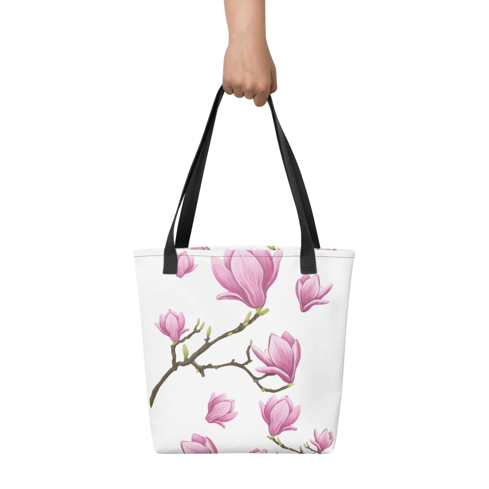 Magnolia all-over print tote bag with black handles held by a hand
