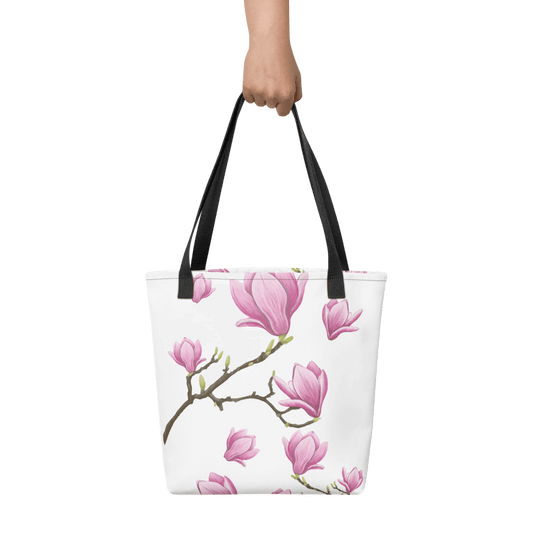 Magnolia all-over print tote bag with black handles held by a hand
