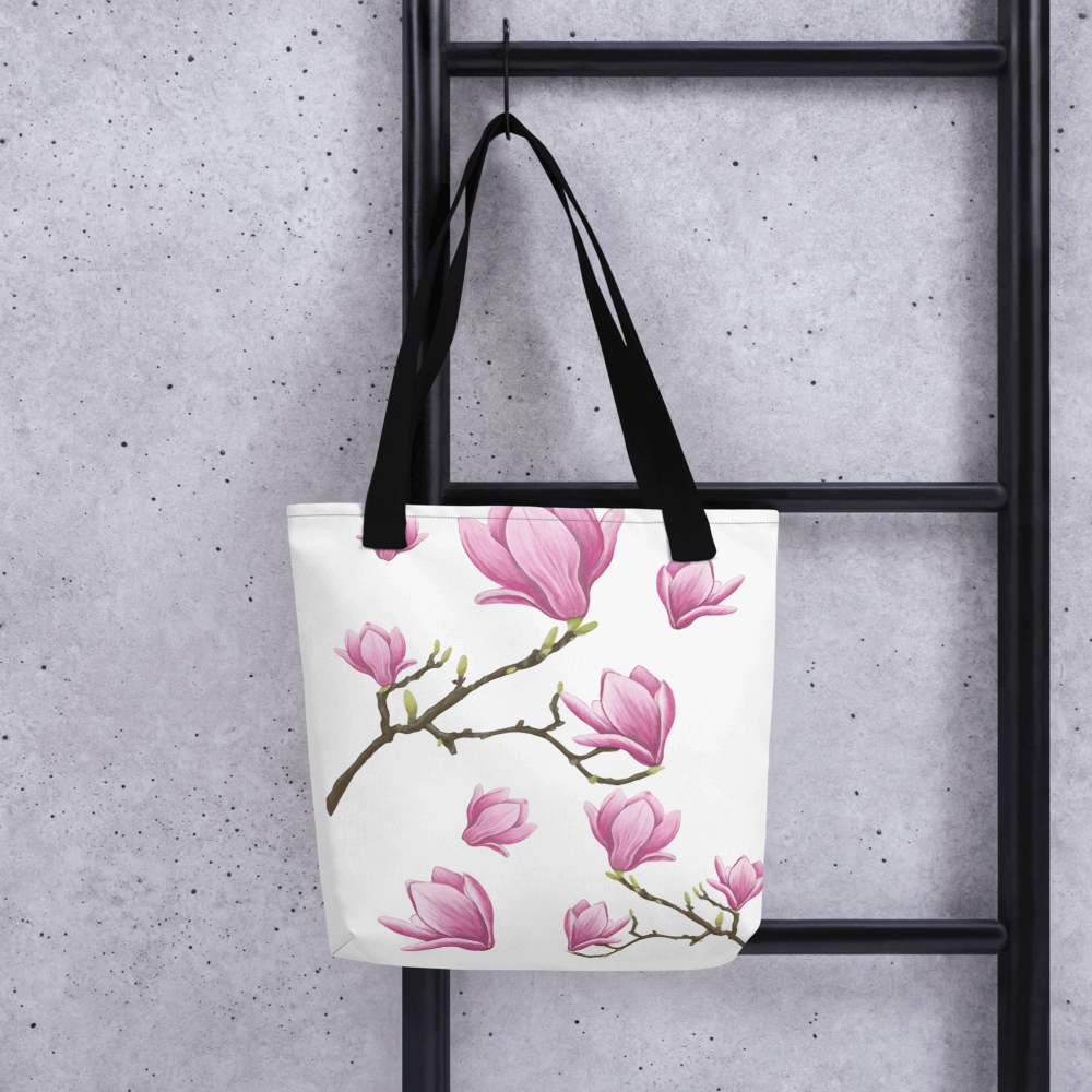 Magnolia all-over print tote bag with black handles hanging on a ladder
