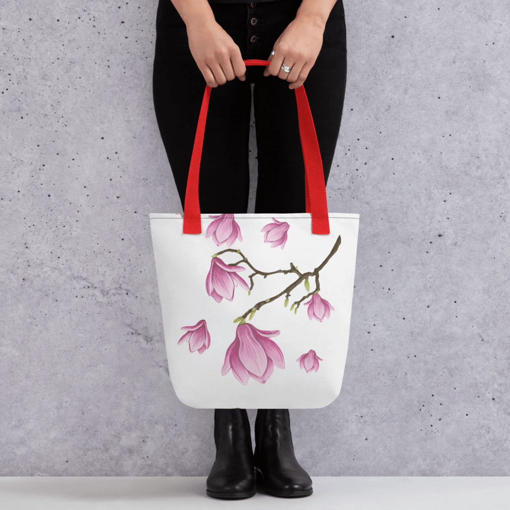 Magnolia all-over print with red handles held by a person dressed in black with both hands holding it in front
