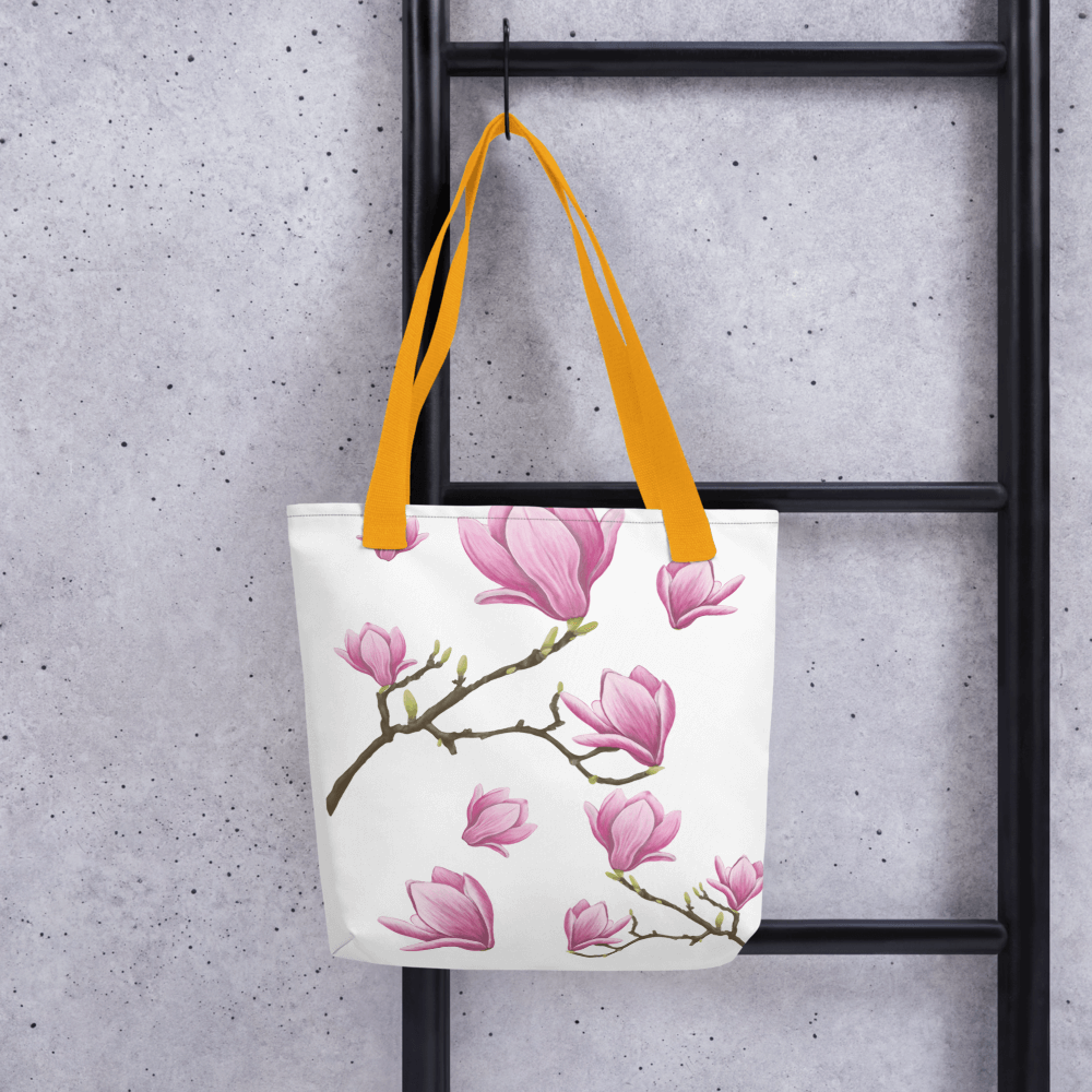 Magnolia all-over print tote bag with yellow handles hanging on a ladder
