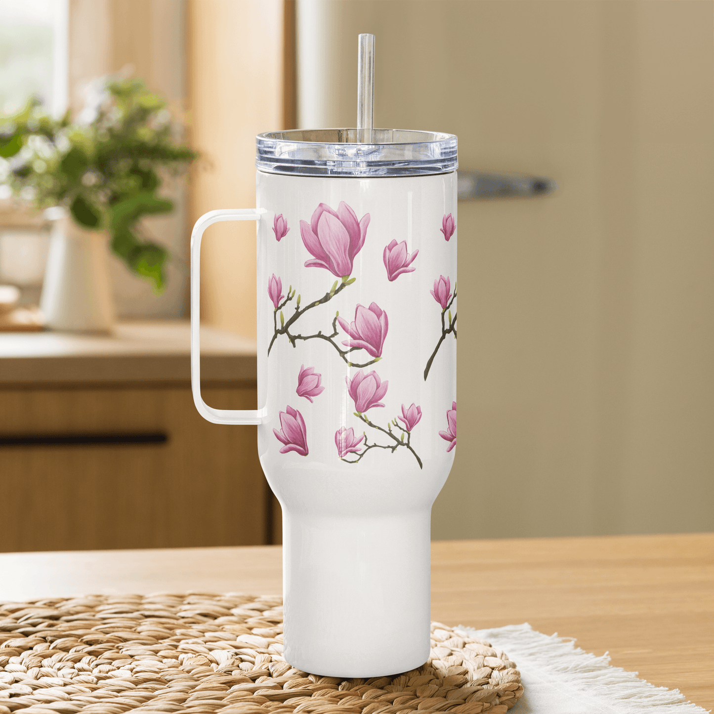 Magnolia design 25oz tumbler with handle and straw on a table, perfect for travel and outdoor hydration.