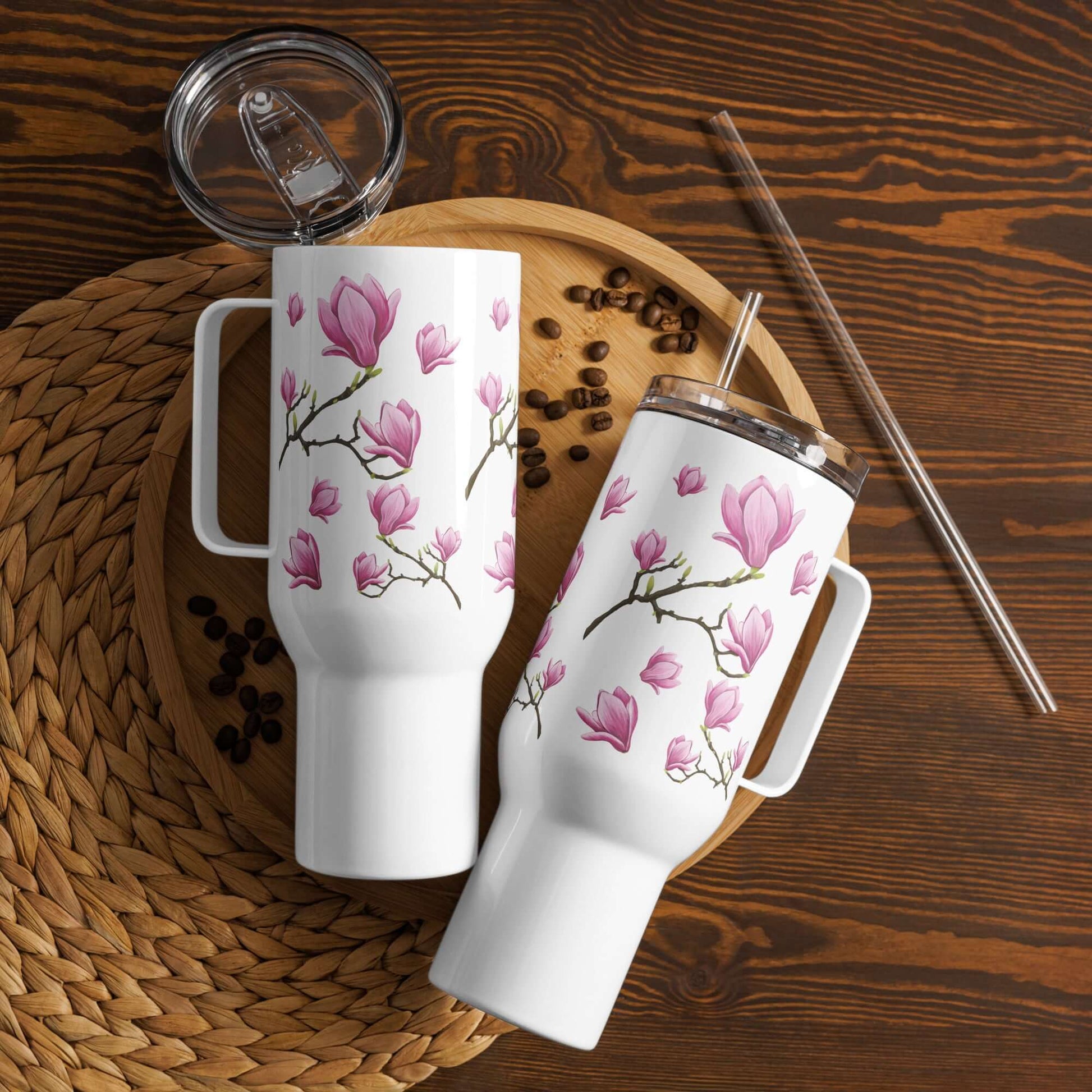 Magnolia design tumblers with handles on a wooden surface, ideal travel mugs for coffee and hydration.