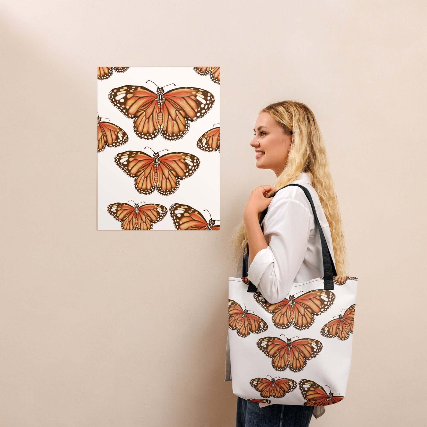 Woman holding a butterfly migration canvas tote bag against a wall art display of monarch butterflies.