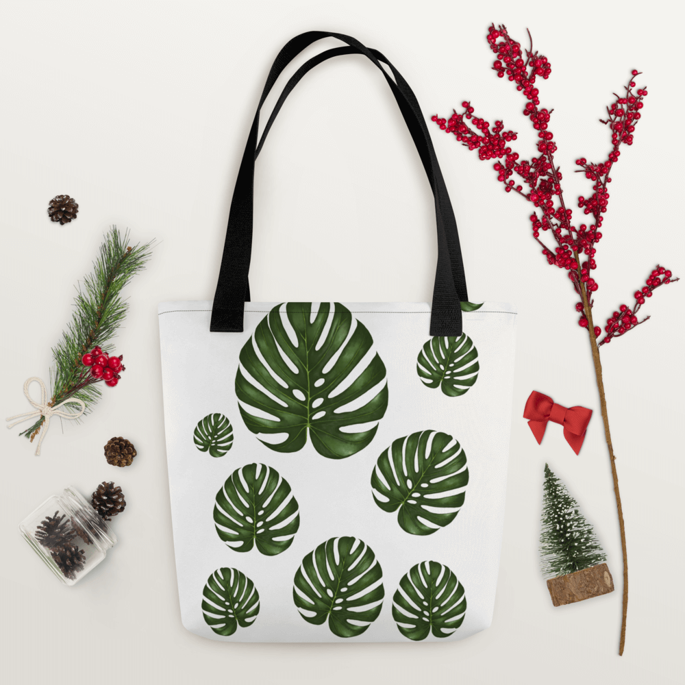 Monstera all-over print tote bag with black handles within Christmas decorations like red berry little branch