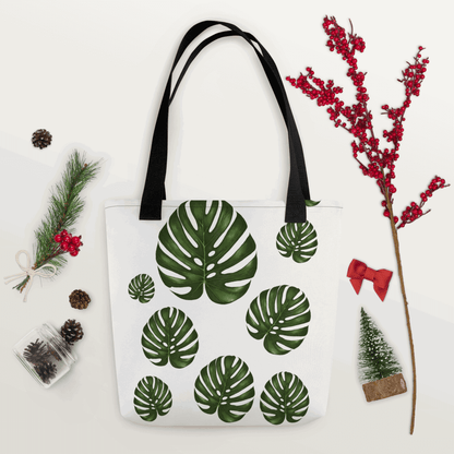 Monstera all-over print tote bag with black handles within Christmas decorations like red berry little branch