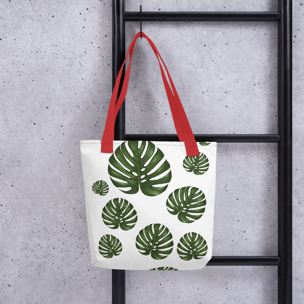 Monstera all-over print tote bag with red handles hanging on a ladder