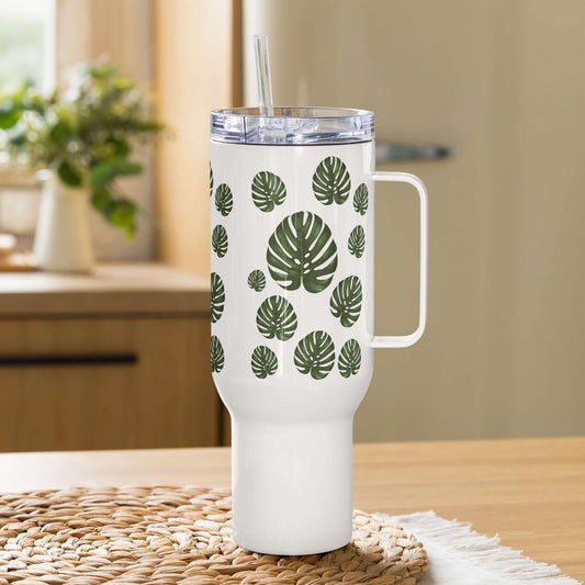 Monstera design tumbler with handle and straw on a wooden table, perfect for hydration and style.