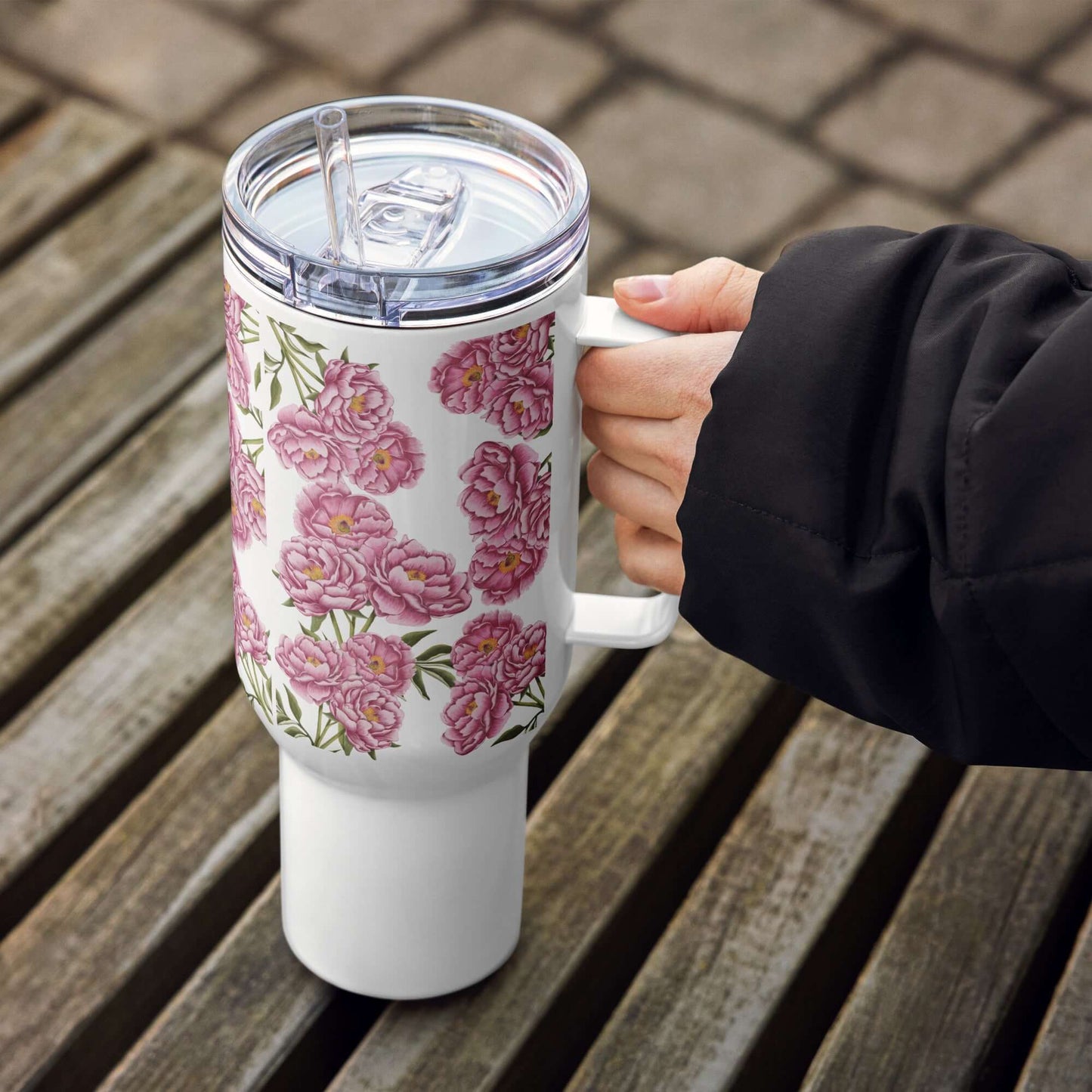 Peony design insulated tumbler in hand, showcasing floral pattern and straw on a wooden table. Perfect for travel and hydration.