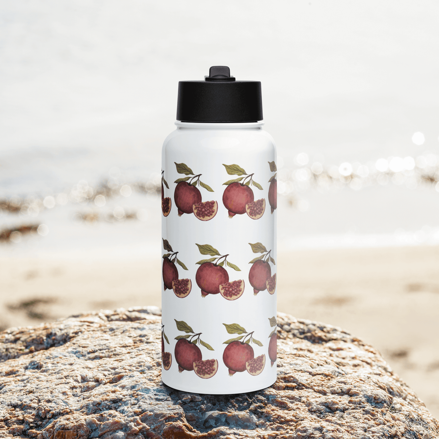 Vibrant pomegranate stainless steel water bottle on a rock by the beach, perfect for hydration adventures.