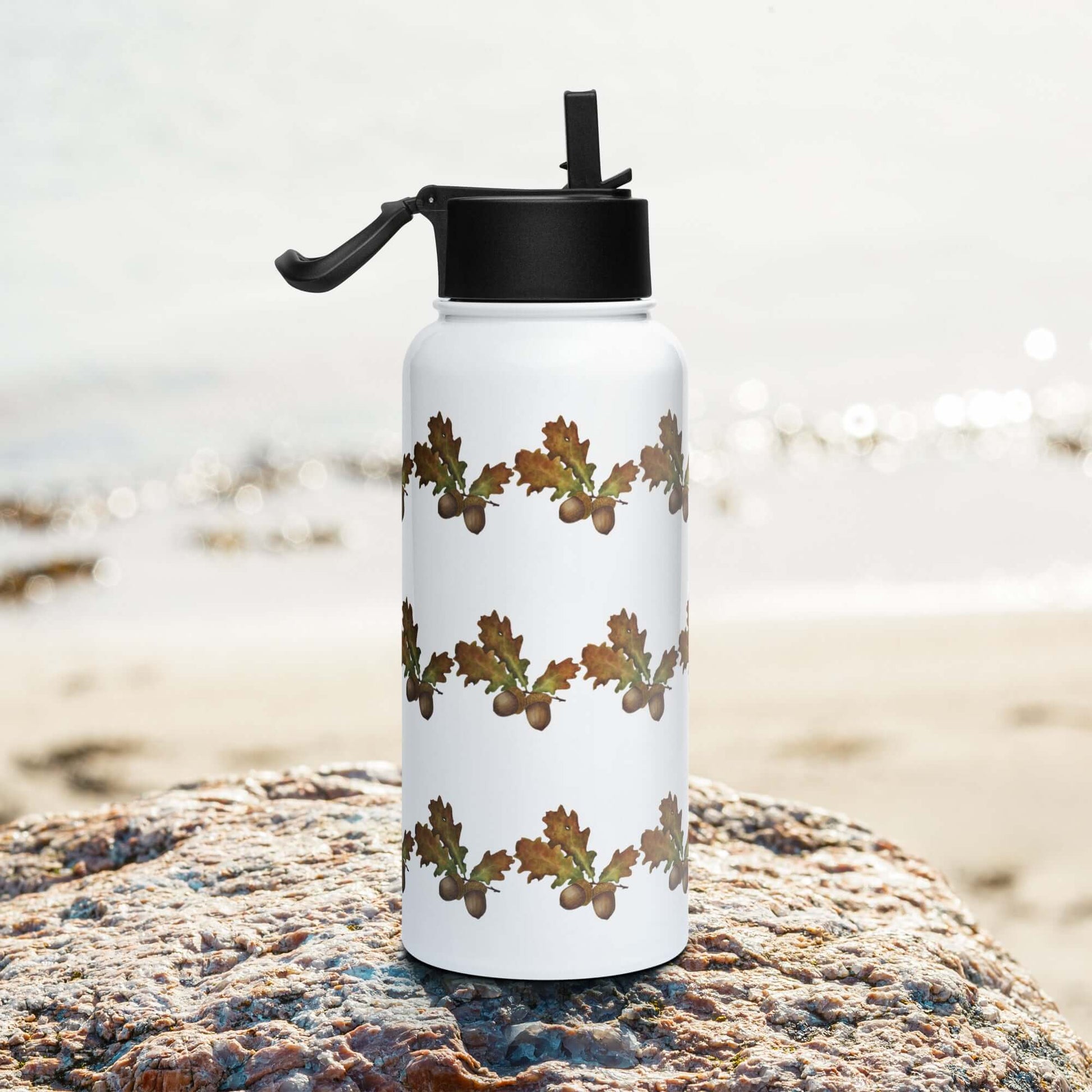 Oak-themed insulated tumbler on a rock by the beach, perfect for outdoor activities and personalized gifts.