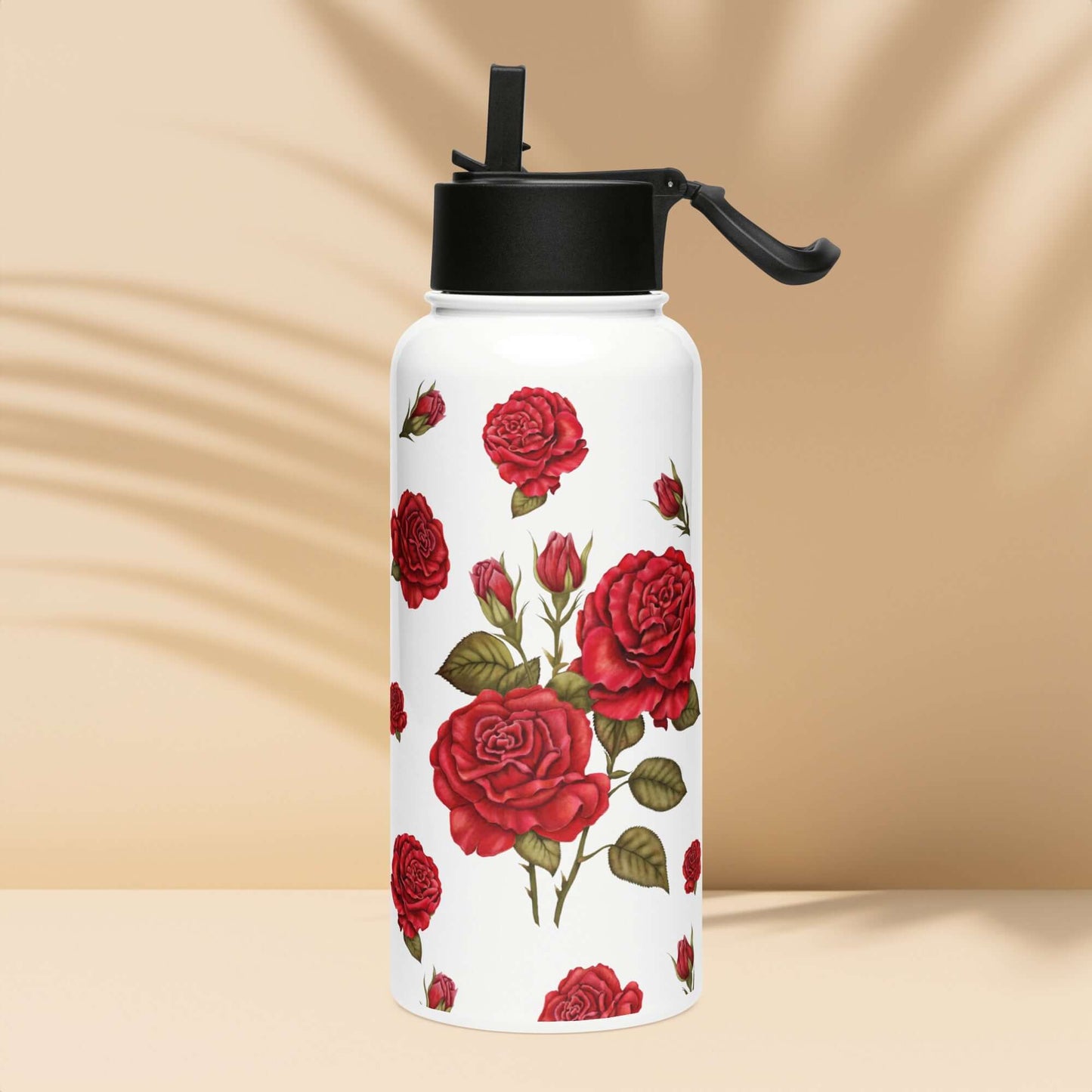 A rose-adorned water bottle rests on warm sand, the vibrant yet romantic red rose design harmonizing with the surrounding coastal landscape.