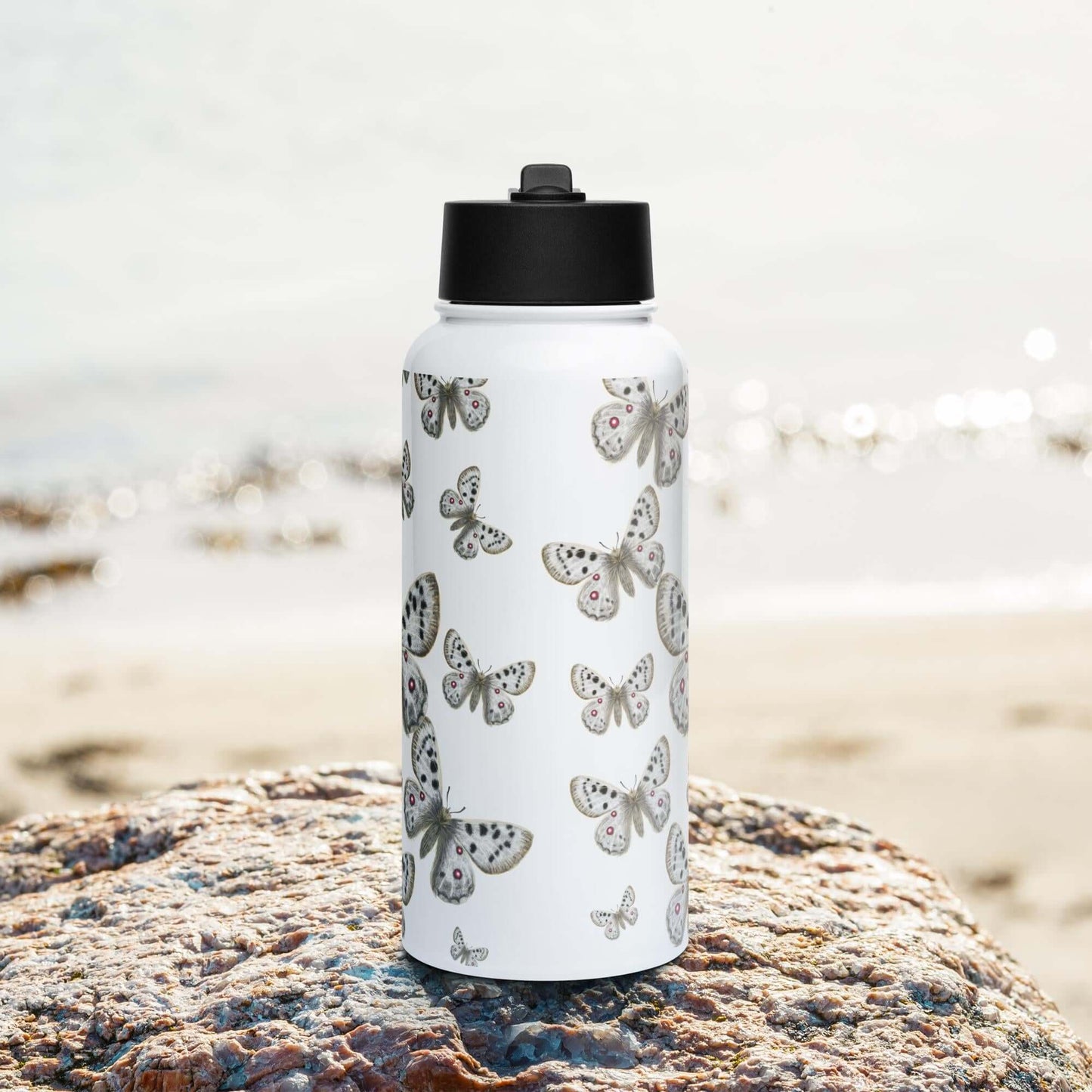 Front view on the beach: Sleek stainless steel water bottle with straw lid, showcased on a sunny beach.