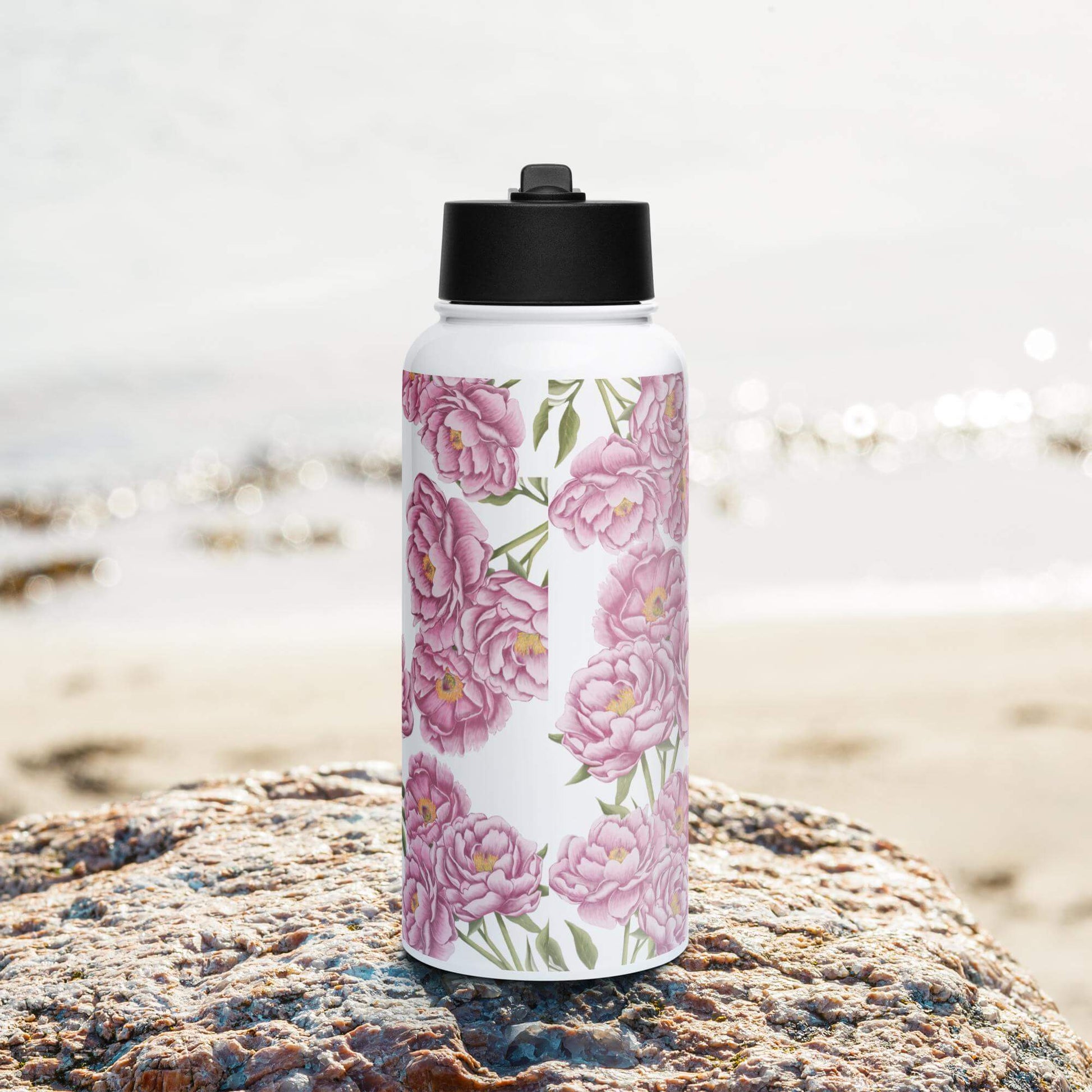 Front view on the beach: Romantic peony-inspired stainless steel water bottle with straw lid, perfect for a day at the beach.