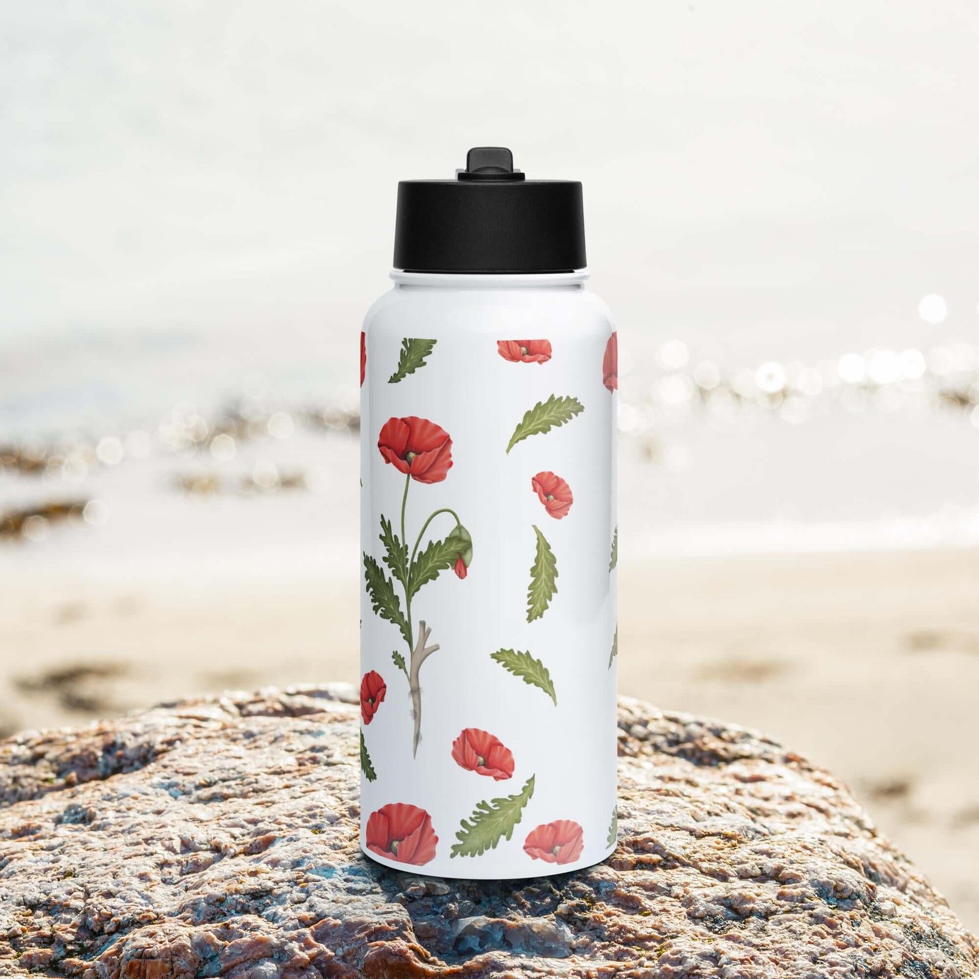 Front view on the beach: Vibrant poppy-inspired stainless steel water bottle with straw lid, perfect for a day at the beach.